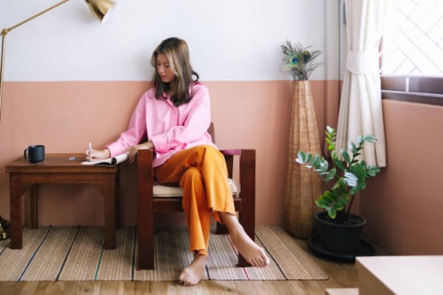a serious beautiful businesswoman in pink shirt and orange trousers taking notes while relaxing at home - home decoration stockfoto's en -beelden