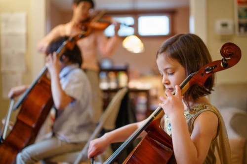 a small child plays cello concert with her family in the living room - concert stock pictures, royalty-free photos & images