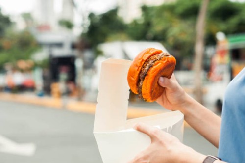 a southeast asian woman is holding a hamburger with paper container and food truck background - junk food stock pictures, royalty-free photos & images