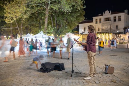 a street musician plays and sings to passers-by in a square of a small resort town. - concert stock pictures, royalty-free photos & images