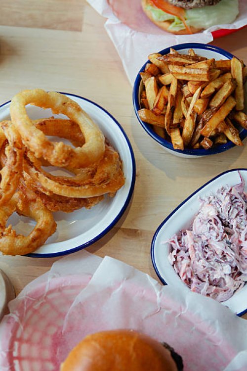 a table full of junk food, burgers, onion rings - junk food fotografías e imágenes de stock