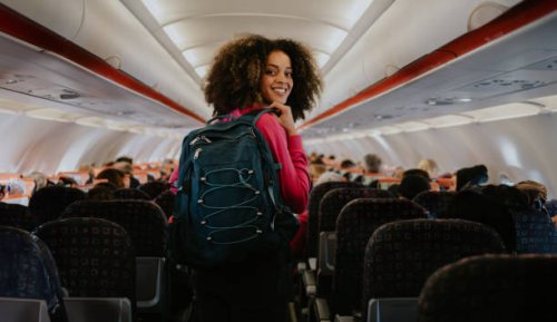 a woman boards a commercial aircraft with hand luggage. she glances over her shoulder and smiles at the camera. - travel stock pictures, royalty-free photos & images