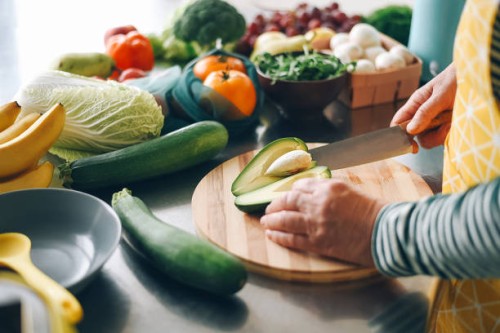 a woman cuts a ripe avocado and takes out a stone from it on a wooden plank. fresh vegetables. salad preparation. diet food. ecological products. - food stock pictures, royalty-free photos & images