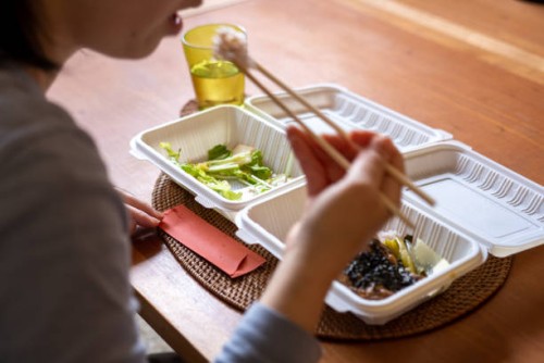 a woman eating a take-out lunch box at her table at home. - junk food stock pictures, royalty-free photos & images