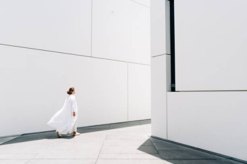 a woman in a white dress walks near a white minimalist building. - fashion stock pictures, royalty-free photos & images