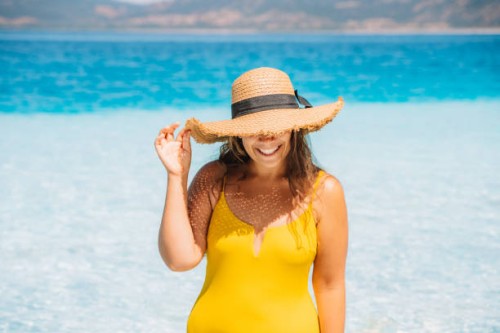a woman in a yellow swimsuit and straw hat emerges from the sea with clear turquoise water on a summer sunny day. - fashion stock pictures, royalty-free photos & images