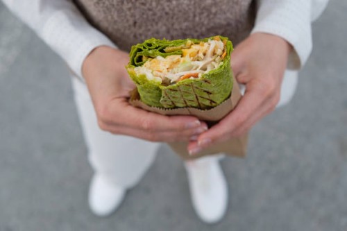 a woman or a girl, a high school student, eats vegetarian or vegan vegetable shawarma on the street. the concept of fast food, takeaway food. lush, burrito, roll in the hands of a woman. junk food, snacks. sustainable develop