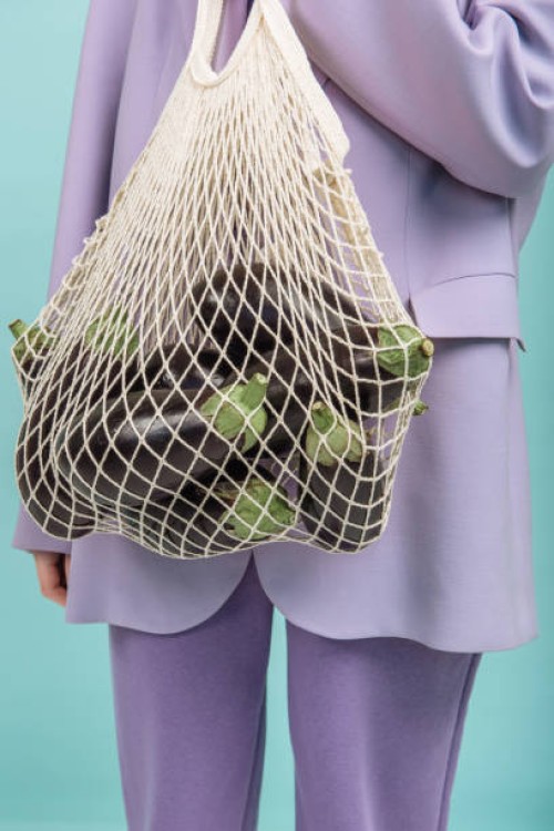 a woman's hand holds a string bag with eggplant on a colored background - fashion stock pictures, royalty-free photos & images