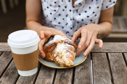a woman with polka dot shirt, eating a croissant - junk food stock pictures, royalty-free photos & images