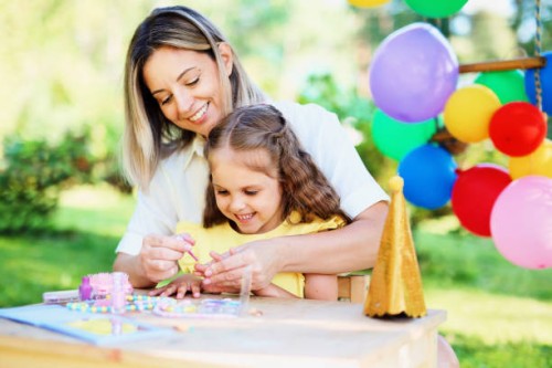 a young cheerful mom is having fun with her child, teaching the baby to paint her nails on her birthday - garden decoration stock pictures, royalty-free photos & images