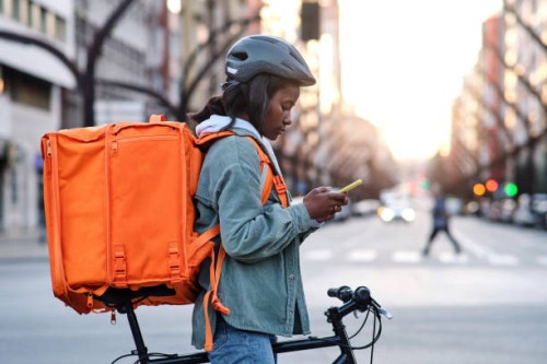 a young delivery woman on her bicycle looking on her smartphone for the route of her delivery - food stock pictures, royalty-free photos & images