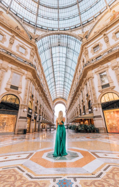 a young tourist woman in a green long dress walking, shopping and standing in the galleria vittorio emanuele ii in milan, italy, offers a stunning view of the golden gate to luxury shopping - fashion stock pictures, royalty-f
