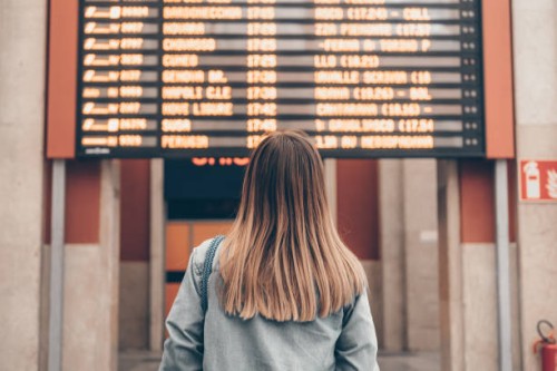 a young woman at a railway station or at the airport looks at the smartphone screen against the background of the arrival and departure board - travel photos et images de collection