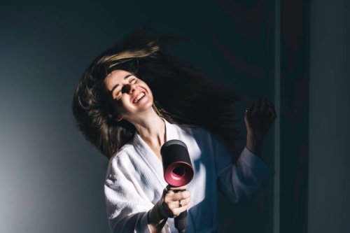 a young woman in white bathrobe blow-dries her hair at home. - hairstyle stockfoto's en -beelden