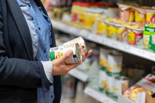 a young woman reads and compares the labels of two cans - junk food stock pictures, royalty-free photos & images
