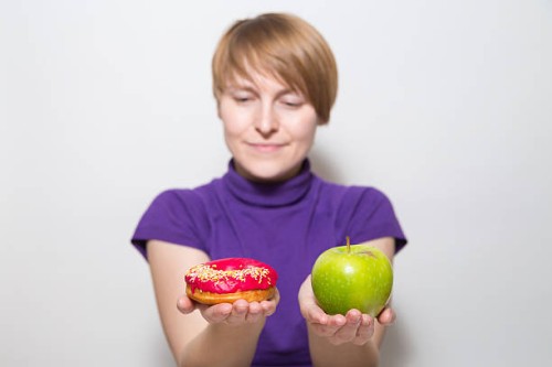 a young woman struggling to choose between an apple and a donut - junk food stock pictures, royalty-free photos & images