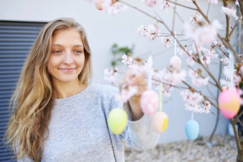 a young woman with blond long hair hangs easter eggs on her cherry tree - garden decoration stock pictures, royalty-free photos & images