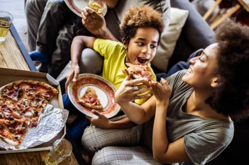above view of black mother feeding her daughter with pizza at home. - junk food stock pictures, royalty-free photos & images