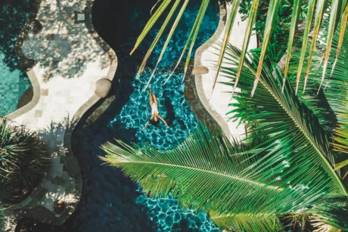 aerial drone view of woman floating on water surface in luxury pool in tropical garden - travel stock-fotos und bilder