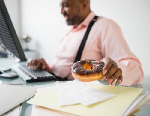 african american businessman eating donut at desk - junk food stock pictures, royalty-free photos & images