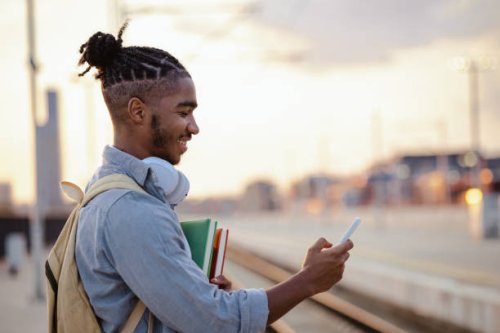 african american male student waiting for a train and checking smart phone - hairstyle stock pictures, royalty-free photos & images