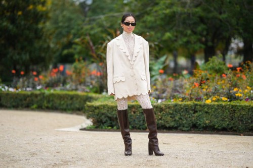 Aimee Song wears black sunglasses from Prada, white pearls earrings, a white lace print pattern high neck / long legging jumpsuit, a white linen...