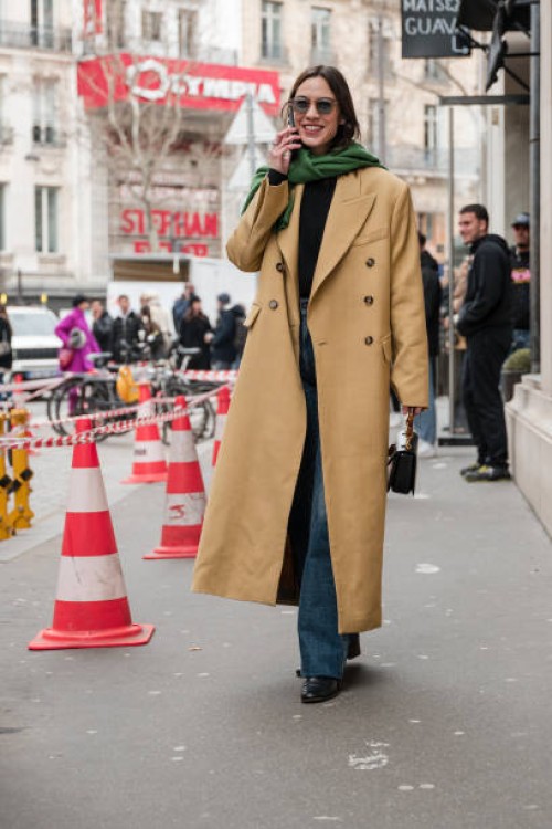 Alexa Chung wears black top, beige coat, green jumper on the shoulders, jeans, black Gucci bag, outside The Row, during the Womenswear Fall/Winter...