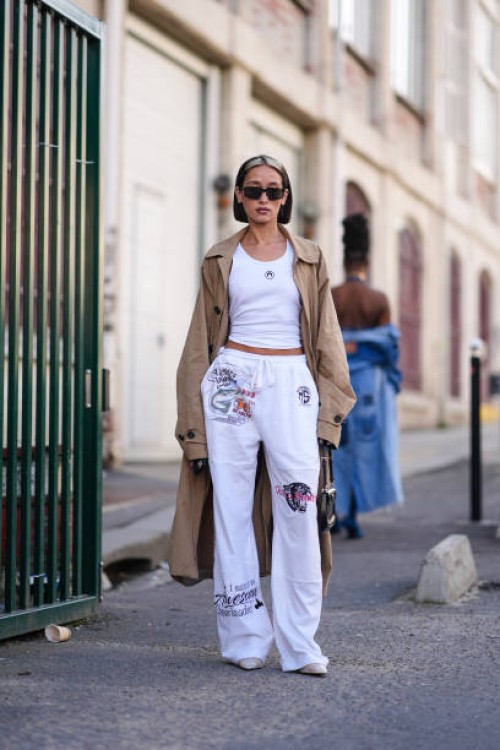 Alexandra Guerain wears sunglasses, a beige trench long coat , a white tank top, wide leg flared pants , outside Marine Serre, during the Womenswear...