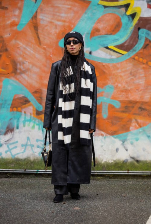 Amaka Hamelijnck wears black white striped scarf, Prada bag, Celine beanie, black coat, leather pants outside Rabens Saloner during the Copenhagen...