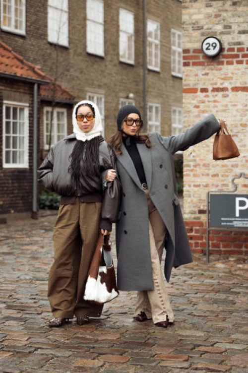 Amaka Hamelijnck wears wide brown pants, dark brown leather jacket, white hat and cow print bag and Benthe Liem wears beige pants, black turtle neck,...