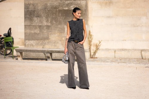 Amalie Gassmann wears a grey knitted vest, grey jeans, Dior belt, black heels and Dior printed bag, outside Dior, during the Womenswear Spring/Summer...