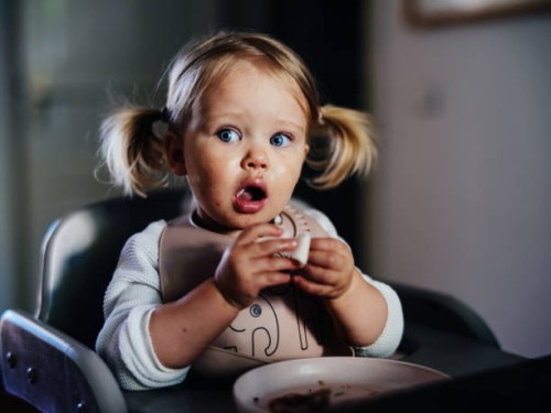 amazed cute toddler girl with pigtails eating at a table at home. - food stock pictures, royalty-free photos & images