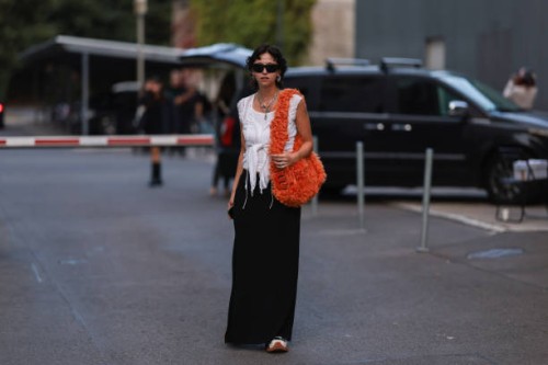 Amelie Kahl is seen wearing black shades, silver earrings and necklaces, white top, fluffy orange Miu Miu shoulder bag, black long skirt and black...
