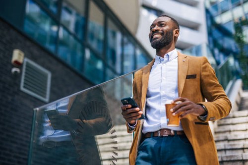 an adult handsome black businessman outside of corporation, using phone - fashion fotografías e imágenes de stock