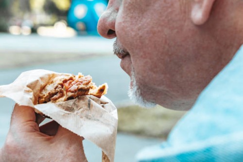 an adult man eating a sandwich on the street. - junk food stock pictures, royalty-free photos & images