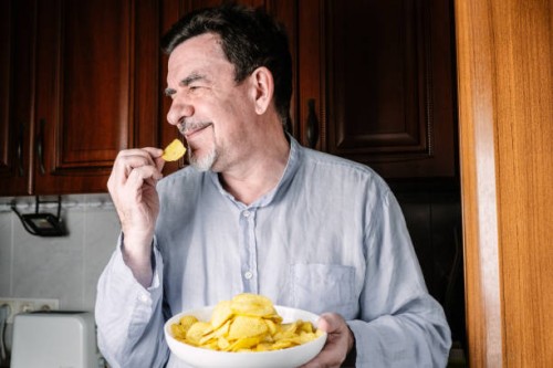 an elderly man eats crisps at home. - junk food stock pictures, royalty-free photos & images