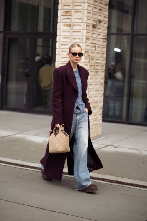 Andrea Steen wears blue jeans, burgundy coat, blue sweater and beige bag outside the Herskind fashion show during the Copenhagen Fashion Week...