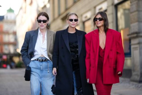 Annabel Rosendahl wears a white shirt, a bicolored gray and brown blazer jacket, a black shiny leather nailed / studded belt, a pale blue faded denim...