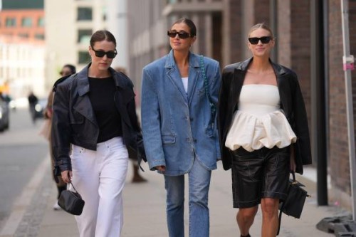 Annabel Rosendahl wears black sunglasses, a black body, a black shiny leather jacket, white wide legs pants, a black shiny leather handbag, Darja...