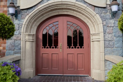 arched entrance door with windows and rustic stone walls, with street lamps and green bushes. - garden decoration stockfoto's en -beelden