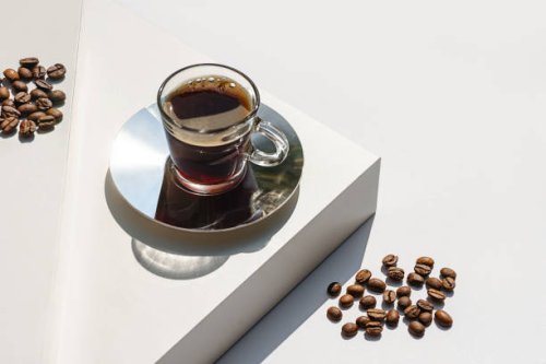 aromatic morning coffee in glass cup and a long shadow from the cup on beige color background. - coffee stock pictures, royalty-free photos & images