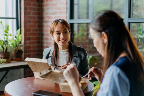asian businesswoman eating take away lunch with her colleague - junk food stock pictures, royalty-free photos & images
