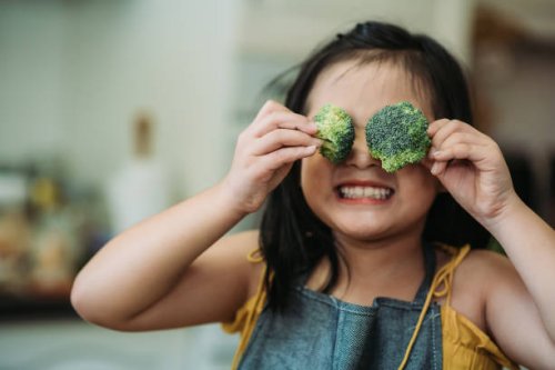 asian chinese female child act cute with hand holding broccoli putting in front of her eyes with smiling face at kitchen - food stock pictures, royalty-free photos & images