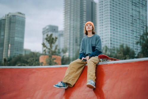 asian chinese female skateboarder sitting at skateboard park looking away - fashion stock pictures, royalty-free photos & images