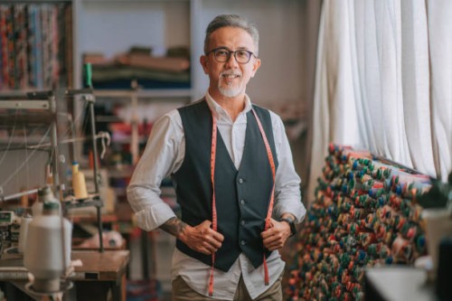 asian chinese senior tailor man with facial hair looking at camera smiling in atelier studio - fashion stock pictures, royalty-free photos & images
