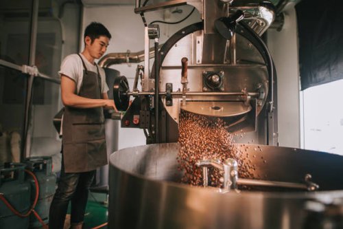 asian craftsperson observing freshly roasted coffee beans being removed from the roaster into the cooling cylinder with motion blur dropping point - coffee stock pictures, royalty-free photos & images