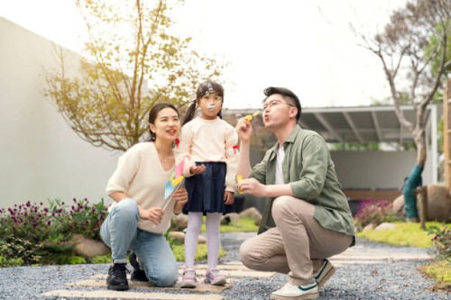 asian little girl playing soap bubbles with her mother and father outdoors. - garden decoration stock pictures, royalty-free photos & images