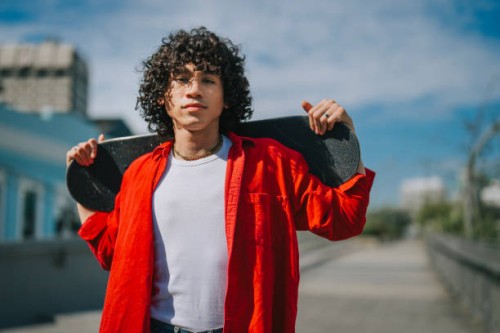 asian malay young man carrying skateboard looking at camera city street weekend morning - fashion stock pictures, royalty-free photos & images