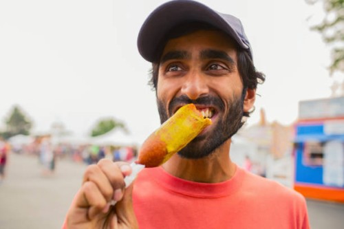 asian man eating corn dog outdoors - food stock pictures, royalty-free photos & images