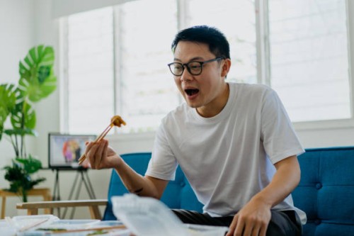 asian man eating home delivery meal in living room - junk food stock pictures, royalty-free photos & images